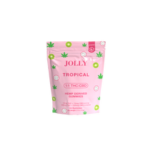 A pink pouch labeled “Jolly Cannabis Tropical Gummies 15mg THC, 15mg CBD” features green cannabis leaves and tropical fruits. Arizona-made, each pack has 15 fruit puree gummies, each with 15mg THC and 15mg CBD.