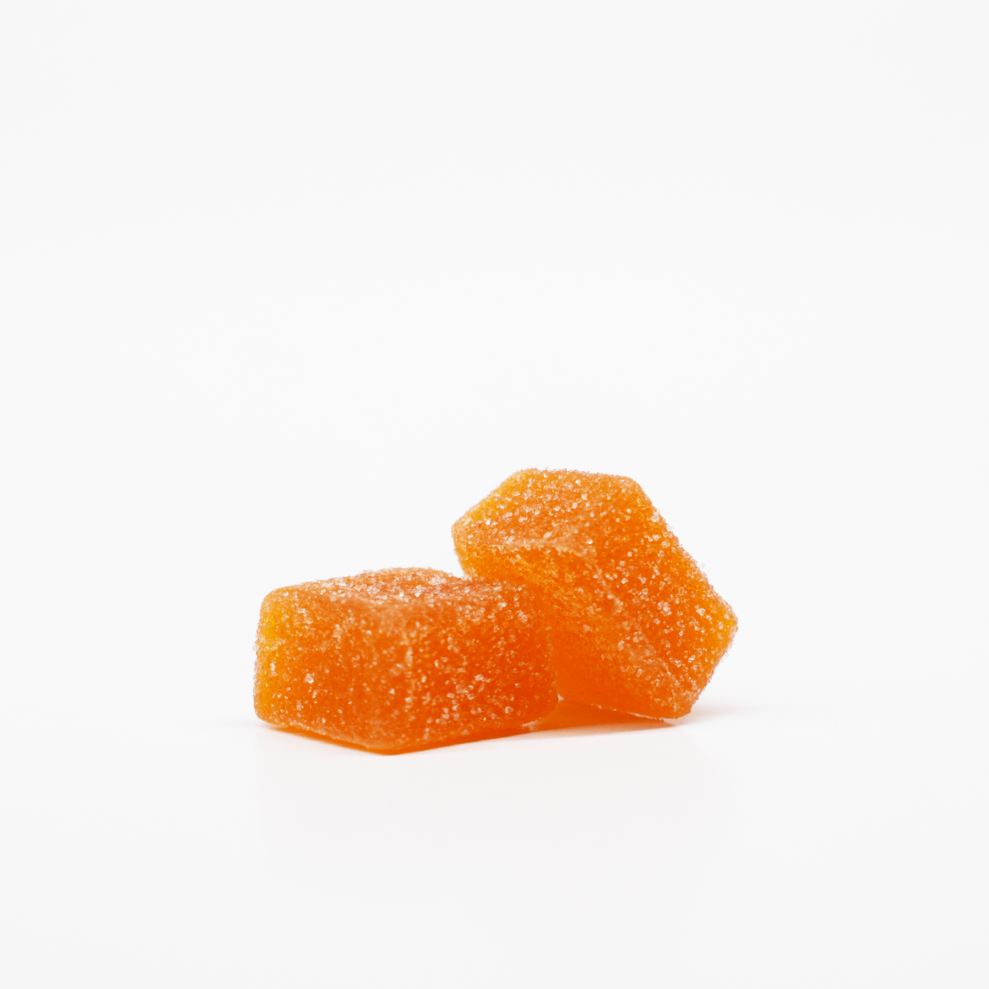 Two Mango Citrus Gummies by Jolly Cannabis, each infused with 15mg THC and 15mg CBD, are stacked on a white background. The rectangular, cushion-shaped orange candies have a sparkling sugar coating and look soft and chewy.