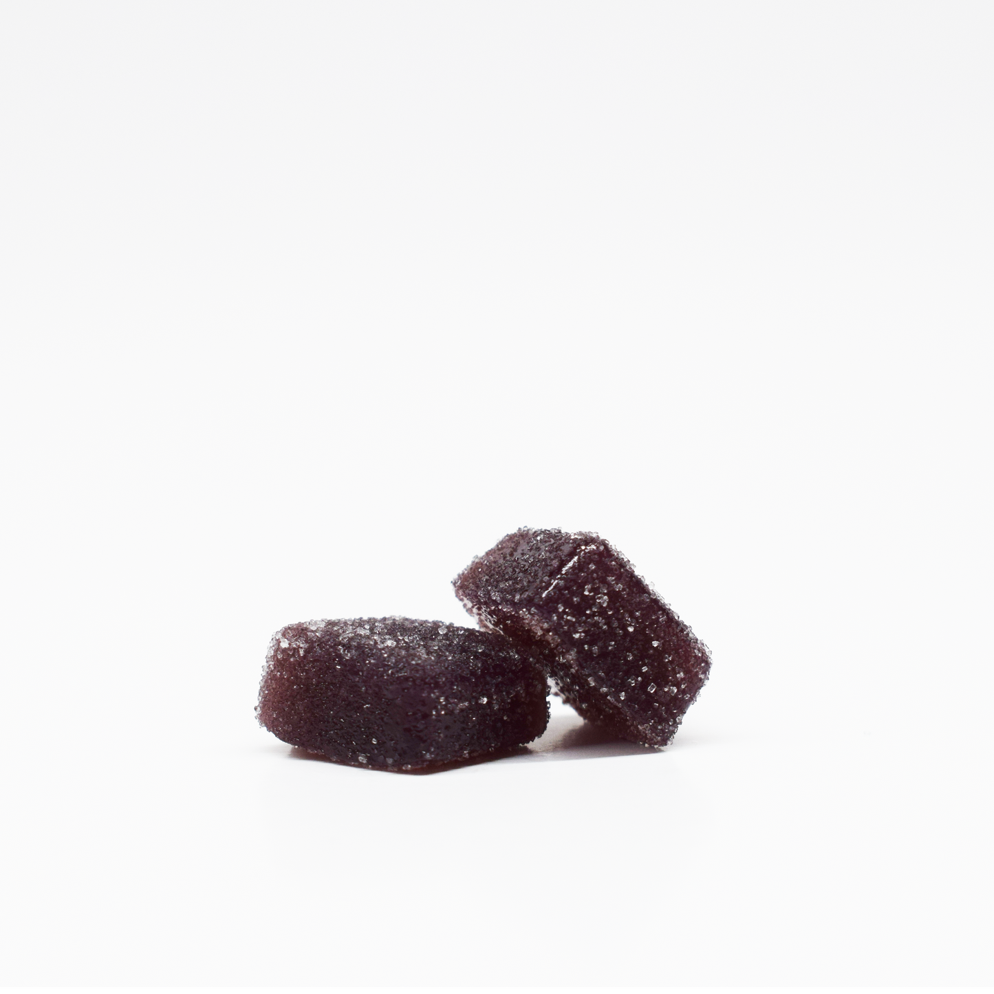 Two dark purple, square-shaped Jolly Cannabis Blackberry Lemon Gummies (5mg THC, 125mg CBD) coated with sugar rest on a white background—one lying flat, the other leaning—showing off their soft texture and sparkly sugar crystal coating.