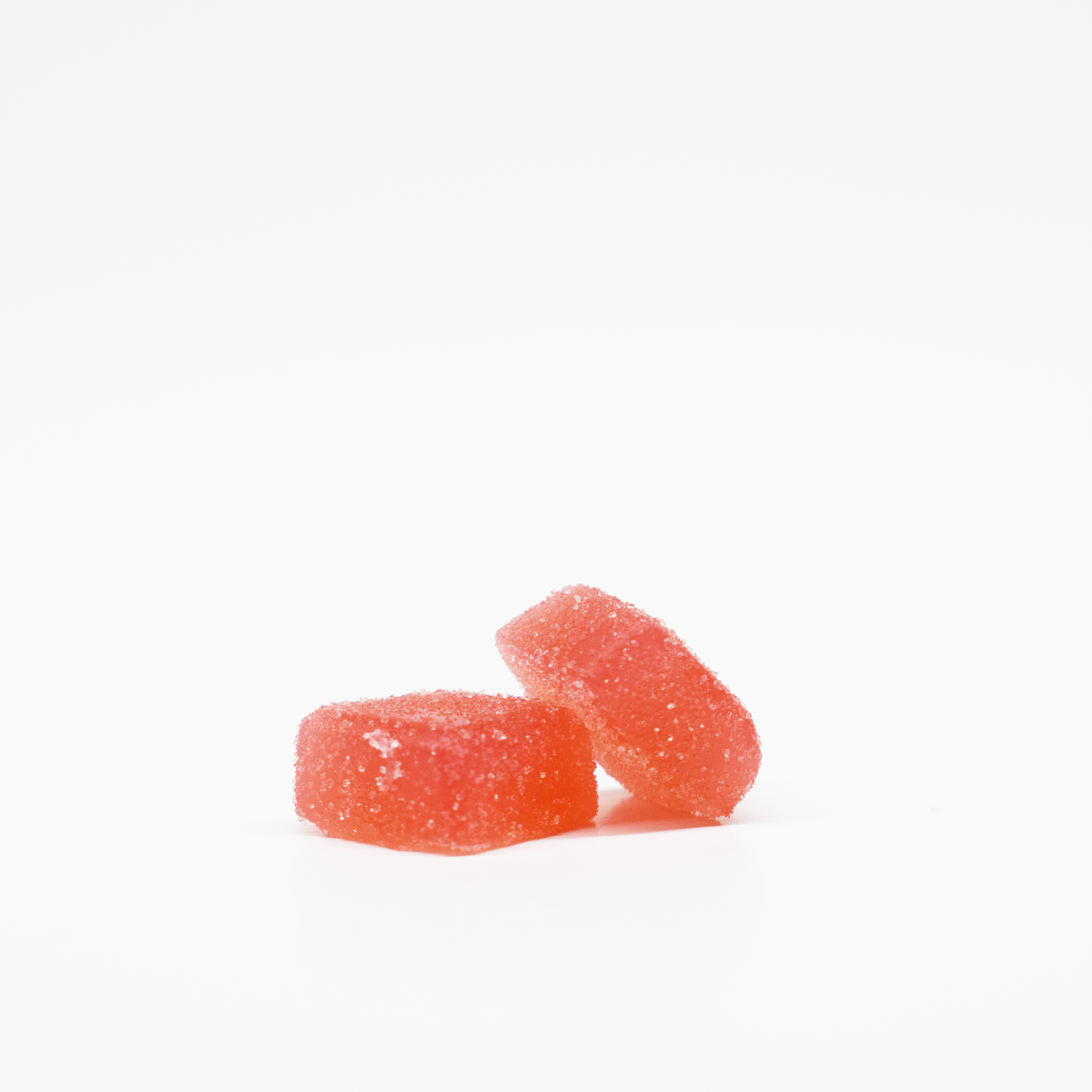 Two red, sugar-coated Fuji Apple Gummies (5mg THC, 125mg CBD) by Jolly Cannabis rest on a white background—one lying flat and the other leaning against it.