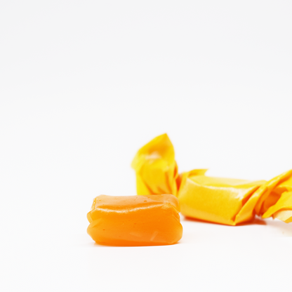 A close-up of two SimplyHemply Orange Passion Fruit Taffy chews (15mg THC, 15mg CBD) on a white background—one unwrapped to reveal its smooth surface, the other in yellow wax paper—positioned at the bottom right of the image.