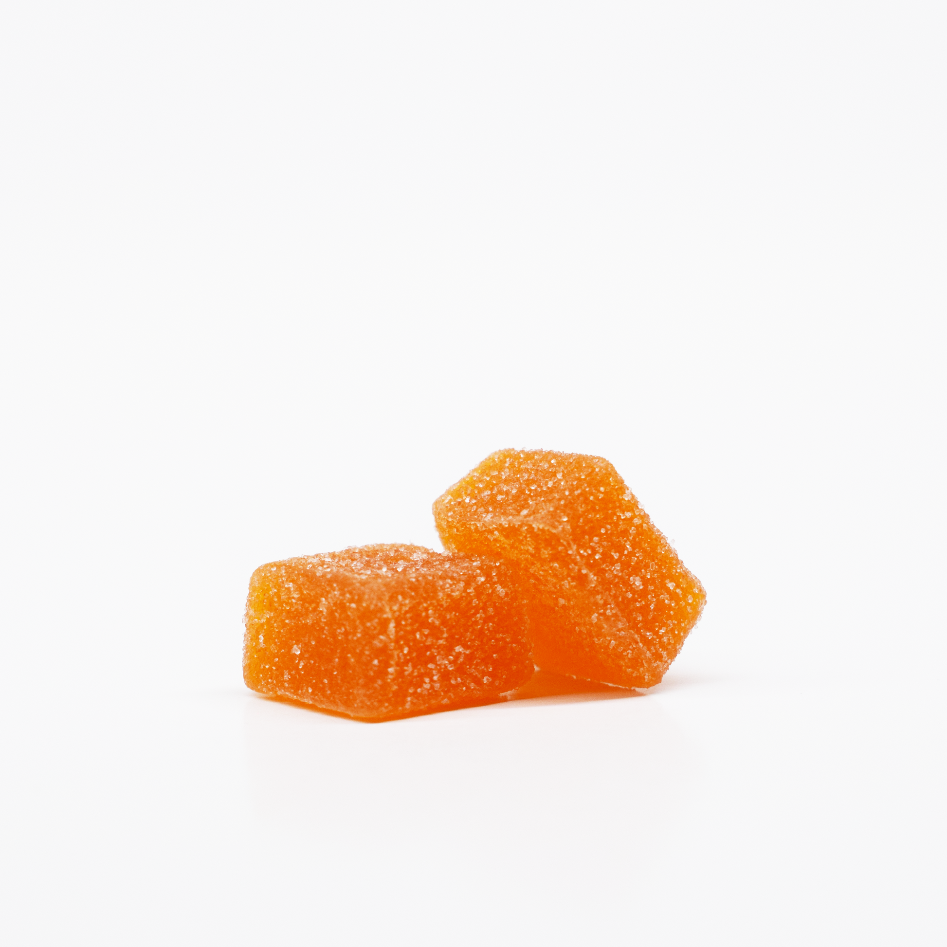 Two Mango Citrus Gummies by Jolly Cannabis, each infused with 15mg THC and 15mg CBD, are stacked on a white background. The rectangular, cushion-shaped orange candies have a sparkling sugar coating and look soft and chewy.