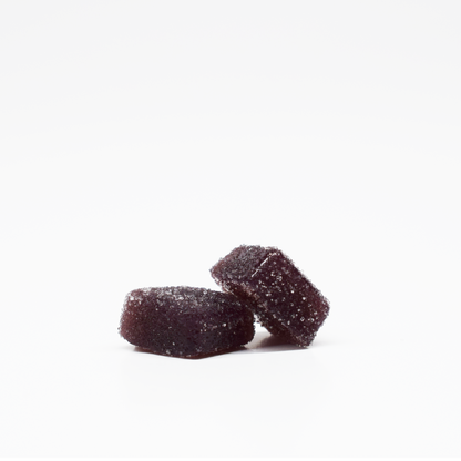 Two dark purple, square-shaped Jolly Cannabis Blackberry Lemon Gummies (5mg THC, 125mg CBD) coated with sugar rest on a white background—one lying flat, the other leaning—showing off their soft texture and sparkly sugar crystal coating.